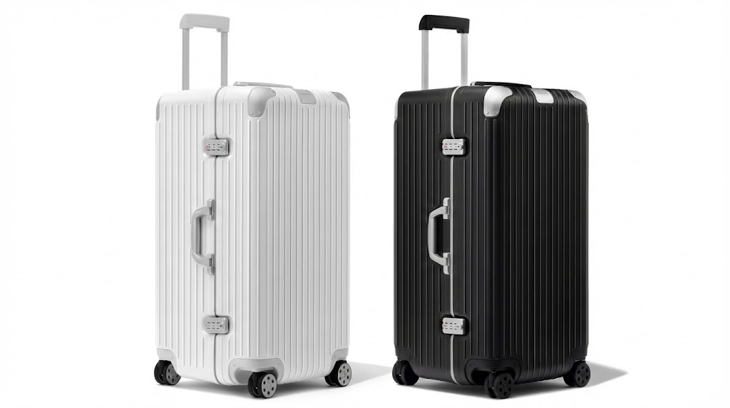RIMOWA Hybrid Trunk Plusスーツケースが2台並列したスタジオ写真。左側はホワイト、右側はブラックのモデルで、共にテレスコープハンドルが引き伸ばされている。長期旅行向けの非常に大きな縦長ボディと、堅牢なアルミニウムの質感が強調されている。
